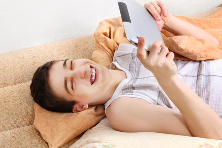 Cheerful Teenager using the Tablet Computer on the Sofa at the Homeの写真素材