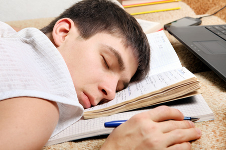 Tired Teenager sleeping with the Books and Laptop on the Sofa at the Home