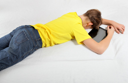 Tired Teenager sleep with the Tablet Computer on the Bedの写真素材