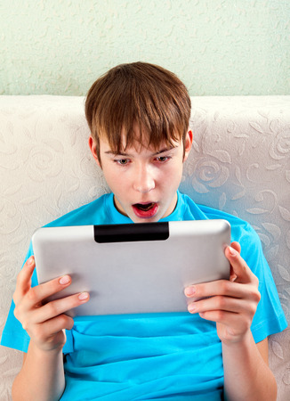 Surprised Teenager with Tablet Computer on the Sofaの写真素材
