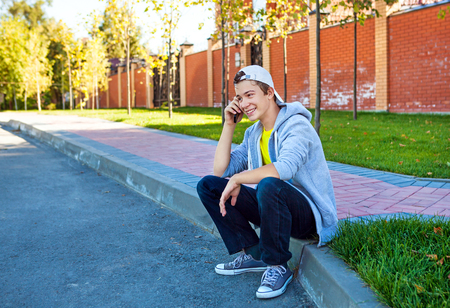 Cheerful Teenager with Cellphone sit on the City Streetの写真素材