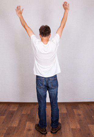 Rear View of the Young Man with Hands Up in the Roomの写真素材