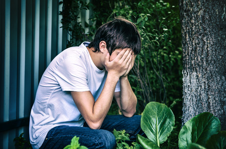Toned Photo of Sorrowful Young Man sit outdoorの写真素材