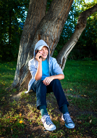 Cheerful Teenager with Cellphone under the Treeの写真素材
