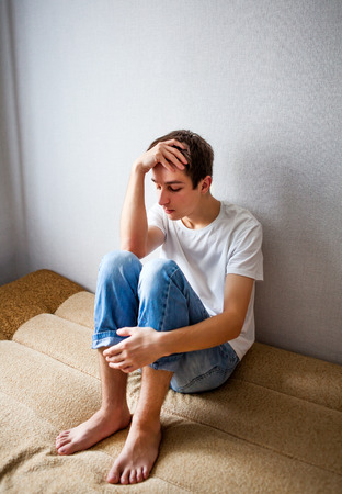 Sad Young Man on the Couch in the Roomの写真素材