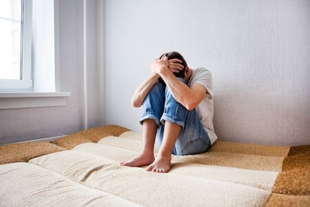 Sad Young Man on the Couch in the Roomの写真素材
