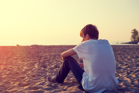 Toned Photo of Pensive Young Man sit on the Sandの写真素材