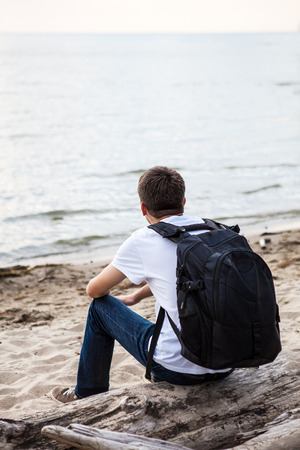 Young Man with Backpack sit on the Log at Seasideの写真素材