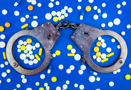 Scattering Pills with a Handcuffs on the Blue Paper Background closeupの写真素材
