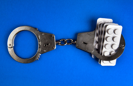 Pills with a Handcuffs on the Blue Paper Background closeupの写真素材