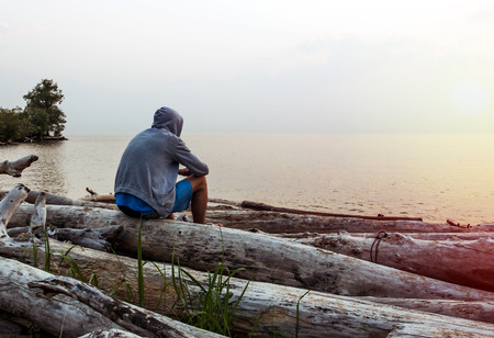 Lonely Young Man in a Hoodie sit on the Sea Backgroundの写真素材