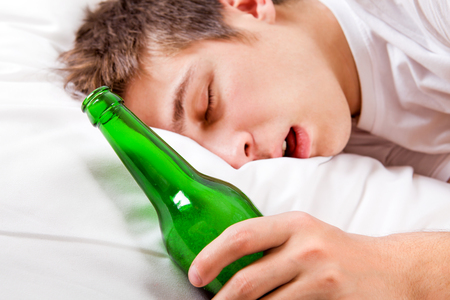 Young Man sleep with a Beer Bottle in the Bed at the Home. Focus on the Bottleの写真素材
