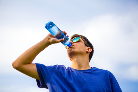 Young Man drinking a Pure Water on the Sky Backgroundの写真素材