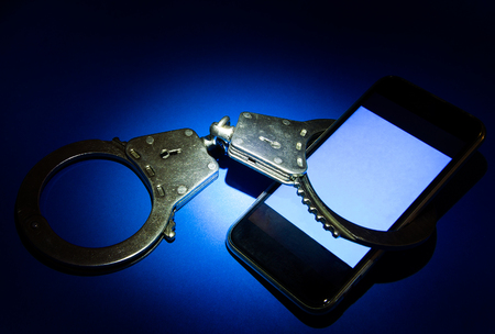 Handcuffs and Mobile Phone on the Blue Paper Background in the Dark closeupの写真素材