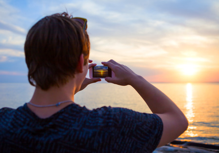 Young Man take a Photo with a Phone at the Seaの写真素材