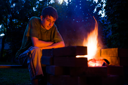 Pensive Young Man sit near the Fire in the Nightの写真素材