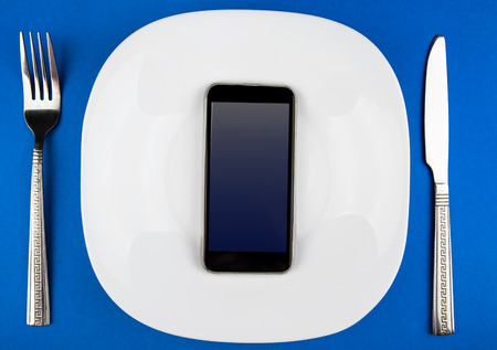 Phone in the Plate with a Cutlery on the Blue Paper Backgroundの写真素材