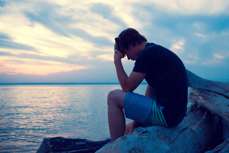 Sad and Lonely Young Man sit at Seaside in the Eveningの写真素材