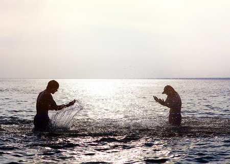 Two People Silhouette with splashes in the Water on the Sunset Backgroundの写真素材