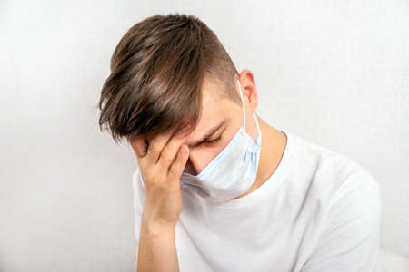 Painful Young Man in a Flu Mask by the Wall in the Room