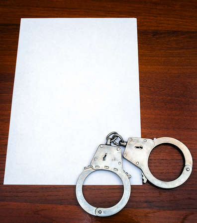 Handcuffs and Blank Paper on the Wooden Table closeupの写真素材