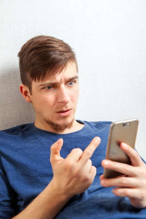 Dissatisfied Young Man show Middle Finger to the Phone by the Wall in the Roomの写真素材