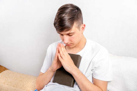 Young Man is Praying with a Book by the White Wall in the Room