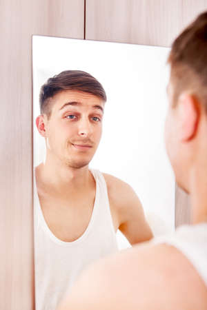 Young Man looking to Reflection in the Mirror in the Roomの写真素材