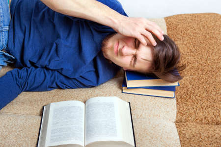 Sleepy and Tired Young Man on the Sofa with a Bookの写真素材