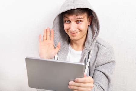 Happy Young Man with Tablet Computer wave with a Hand by the White Wall