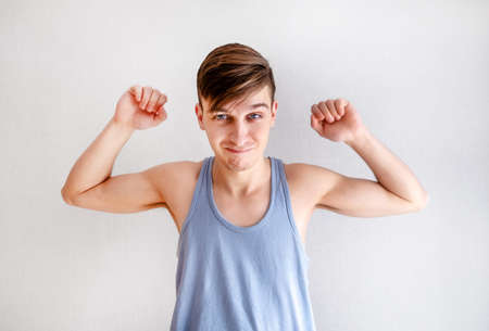 Young Man in Undershirt Muscle Flexing on the White Wall Backgroundの写真素材