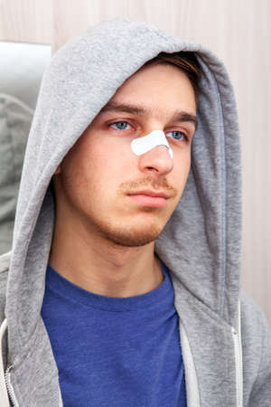 Sad Young Man with a Sticking Plaster on the Nose near the Mirror at the Home