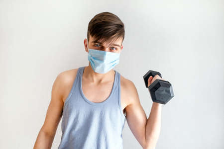 Young Man in Flu Mask hold a Dumbbell by the White Wallの写真素材