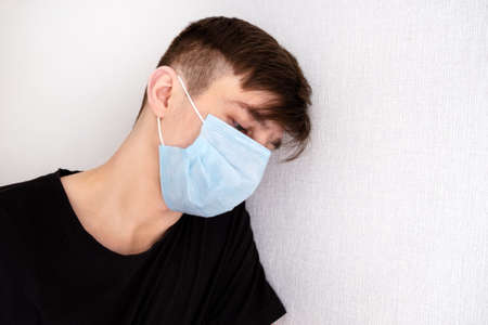 Sad and Tired Young Man in a Flu Mask by the Wall in the Roomの写真素材