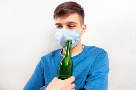 Sad Young Man in Flu Mask with a Beer by the Wall in the Roomの写真素材