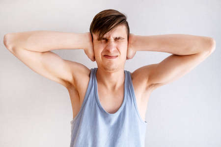 Young Man in Undershirt close the Ears by the White Wall in the Roomの写真素材