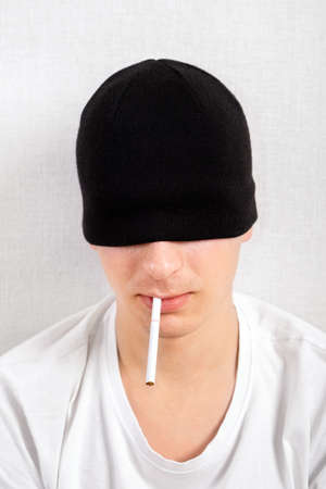 Young Man in a Hat with a Cigarette by the White Wall closeupの写真素材