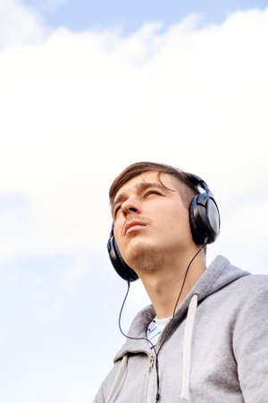 Young Man in Headphones listen to the Music on the Sky Backgroundの写真素材