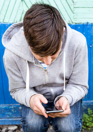Young Man sit with a Phone on the Old Wall Background outdoorの写真素材