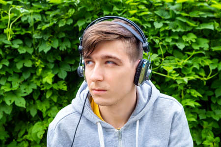 Sad Young Man in Headphones on the Green Leaves Background outdoorの写真素材