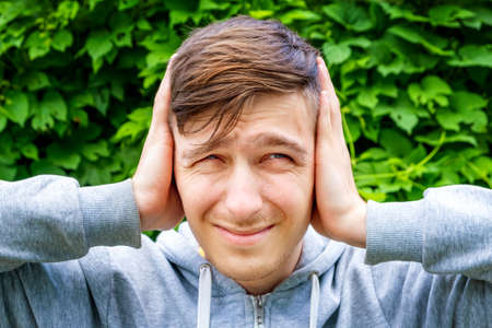 Unhappy Young Man close the Ears on the Green Leaves Background
