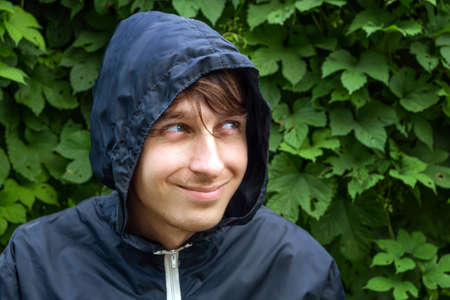 Young Man Portrait in the Raincoat on the Green Leaves Background