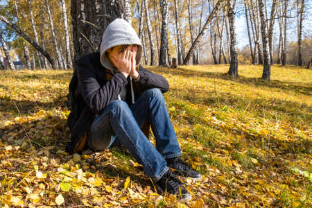 Sad Young Man close his Face and sit in the Autumn Forest Alone