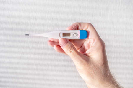 Person hold a Medical Thermometer on the White Wall Background closeup