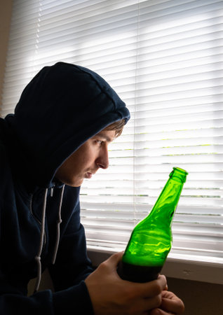 Sad Young Man with a Beer by the Window in the Roomの写真素材