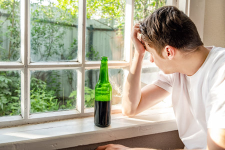 Sad Young Man with a Beer by the Window in the Roomの写真素材