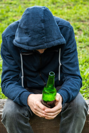 Sad Man in a Hoodie hold a Beer Bottle outdoorの写真素材