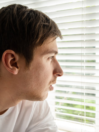 Pensive Young Man by the Window in the Room closeupの写真素材
