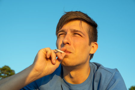 Young Man smoking a Cigarette on the Sky Backgroundの写真素材