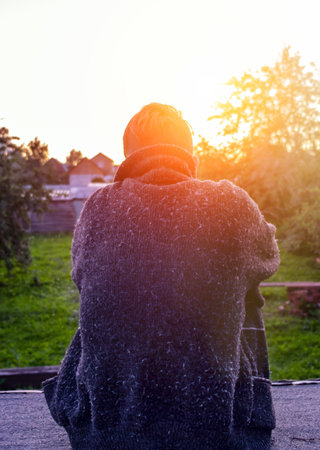 Rear View of a Lonely Man in the Old Sweater sit on the Sunset Background Outdoorの写真素材
